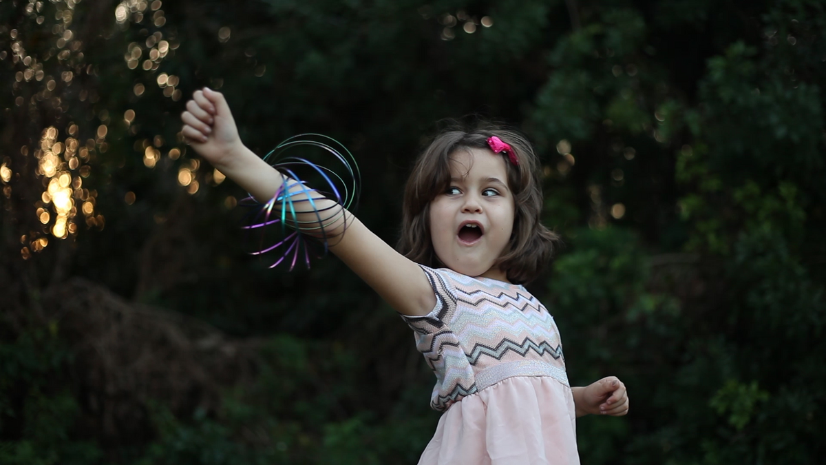 Young girl with toy ring, arm raised outside.